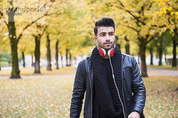 Hübscher junger Mann mit Kopfhörern  der im Herbst gegen Bäume im Park läuft