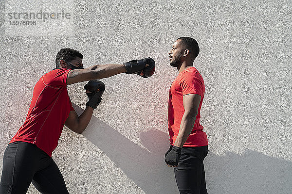 Sportler mit Gesichtsmaske und Boxen gegen einen stillstehenden Trainingspartner