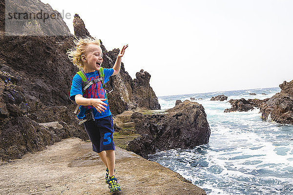 Fröhlicher Junge  der auf einer Felsformation am Meer läuft  während er seinen Urlaub an der Costa Adeje  Kanarische Inseln  Spanien  genießt