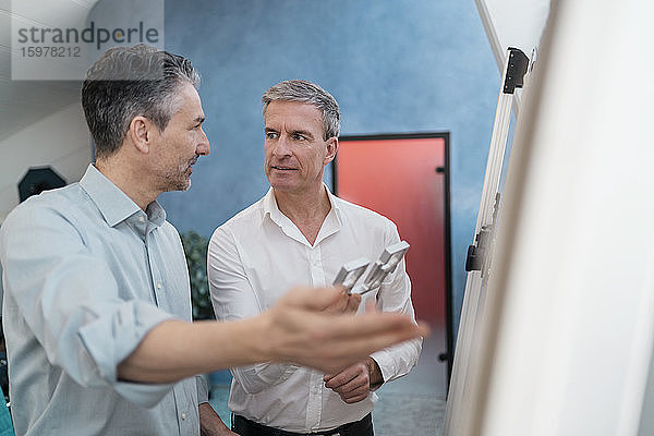 Reife männliche Mitarbeiter diskutieren über Geräte  während sie bei einer Besprechung im Büro am Whiteboard stehen