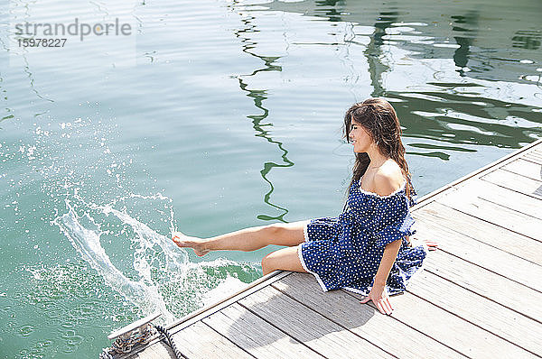Junge Frau spritzt mit den Beinen im Meer  während sie auf einem Steg sitzt