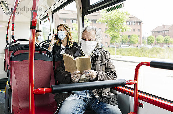 Älterer Mann mit Schutzmaske im öffentlichen Bus beim Lesen eines Buches  Spanien