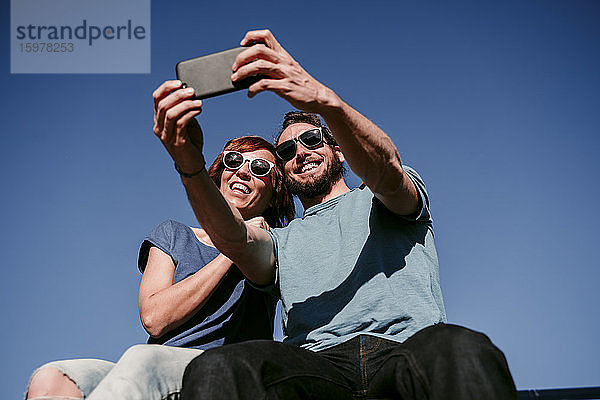 Glückliches Paar nimmt ein Selfie unter blauem Himmel