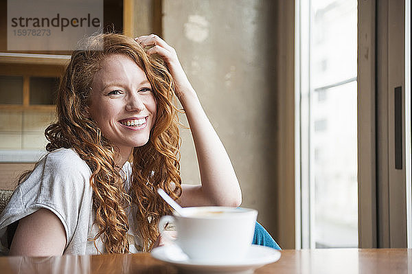Glückliche Frau sitzt am Tisch mit Kaffeetasse zu Hause