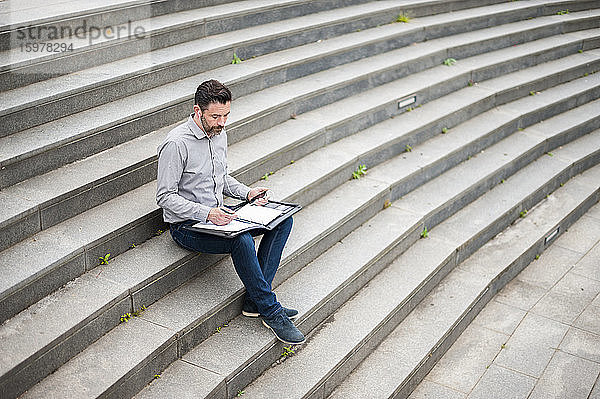 Geschäftsmann in voller Länge  der ein Dokument analysiert  während er auf den Stufen des Amphitheaters sitzt
