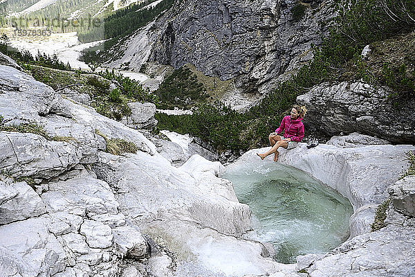 Weibliche Touristin genießt beim Spritzen von Wasser mit dem Bein im Bach gegen den Berg