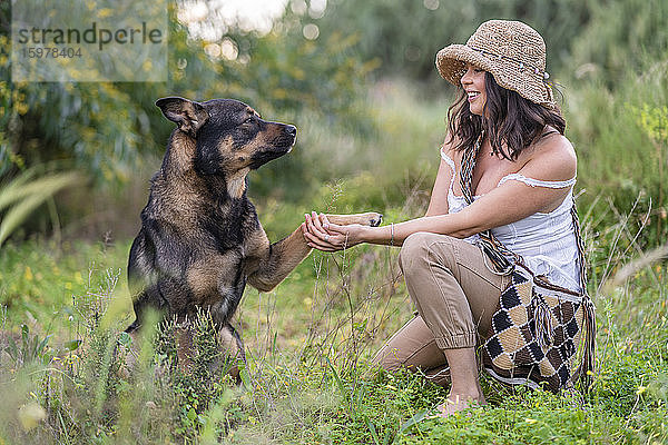 Hund schüttelt Pfote mit schöner junger Frau  die auf Pflanzen kniet  Alicante  Provinz Alicante  Spanien