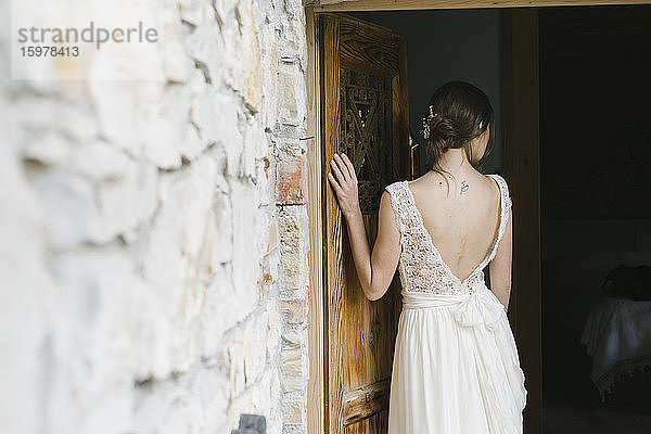 Rückansicht einer Frau im eleganten Hochzeitskleid an der Tür