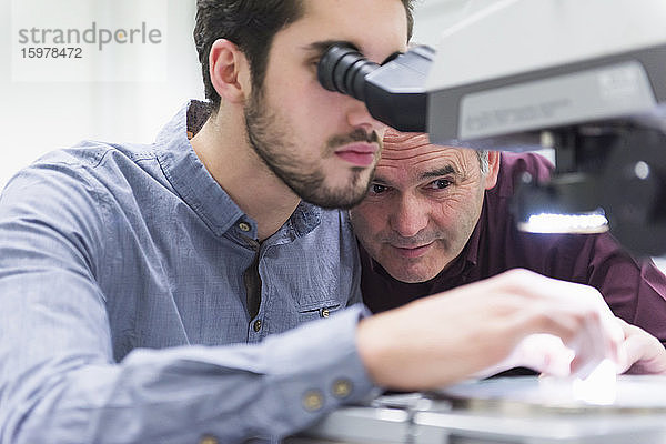 Mann schaut durch ein Mikroskop in einer Fabrik