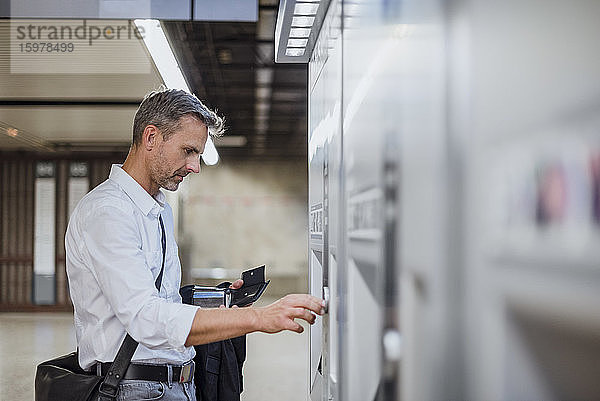 Geschäftsmann beim Geldabheben am Geldautomaten im Bahnhof