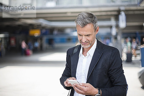 Geschäftsmann  der ein Smartphone benutzt  während er am Bahnhof steht