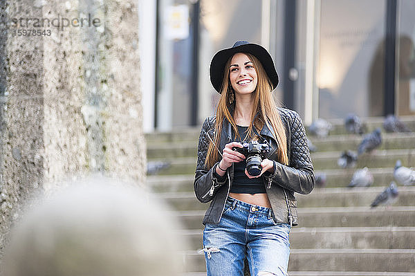 Glückliche junge Frau hält DSLR-Kamera auf Stufen in der Stadt