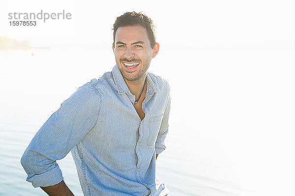 Porträt eines lachenden jungen Mannes vor einem See