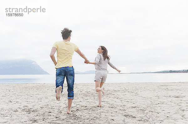 Glückliches Paar läuft Hand in Hand am Strand  Sardinien  Italien