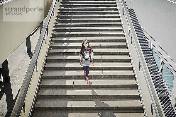 Mädchen mit Maske und Schultasche geht auf einer Treppe