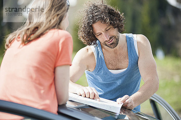 Selbstbewusster  gut aussehender Mann  der mit einer Frau auf dem Autodach eine Karte liest  während eines Sommerausflugs