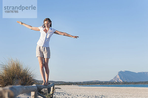 Lächelnde Frau balanciert auf einem Zaun am Strand  Sardinien  Italien