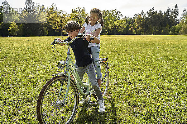 Geschwister genießen eine Fahrradtour im Gras an einem sonnigen Tag