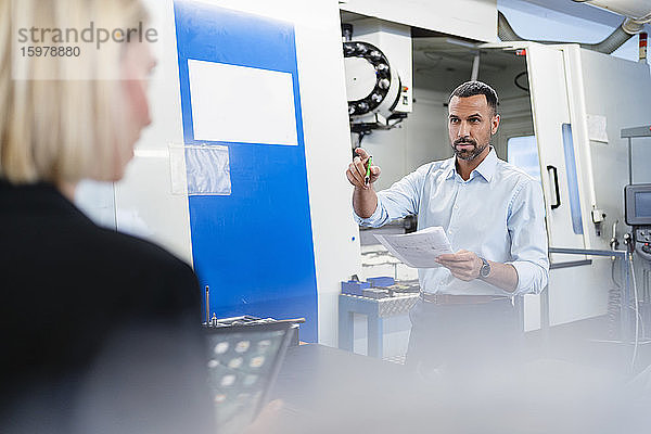 Geschäftsmann mit Plan und Frau in Fabrikhalle