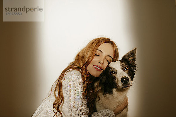 Blonde Frau zu Hause im Pijama  die ihren Border Collie Hund umarmt