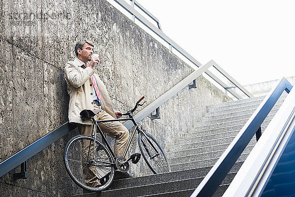 Geschäftsmann trinkt Kaffee  während er mit dem Fahrrad auf einer Treppe steht