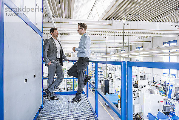 Zwei Geschäftsleute unterhalten sich im oberen Stockwerk einer Fabrik