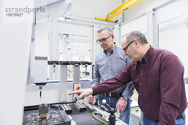 Zwei Geschäftsleute im Gespräch an einer Maschine in einer Fabrik