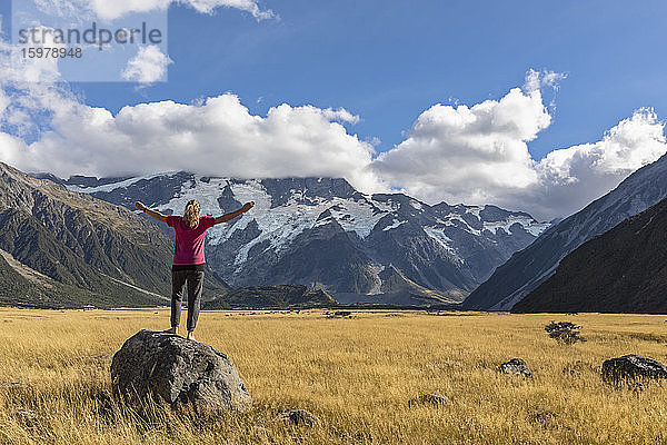 Neuseeland  Ozeanien  Südinsel  Canterbury  Ben Ohau  Südliche Alpen (Neuseeländische Alpen)  Mount Cook National Park  Aoraki / Mount Cook  Frau steht auf Felsblock in Berglandschaft