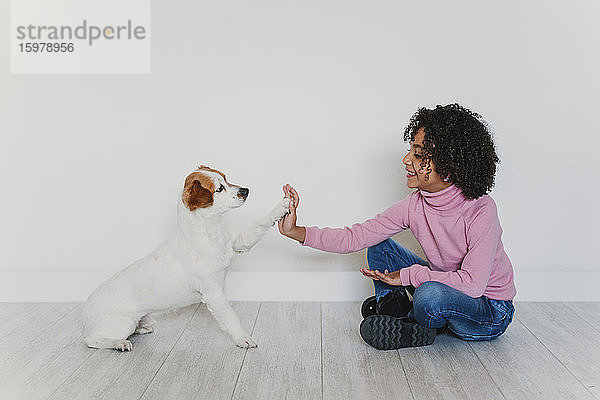 Lächelndes kleines Mädchen sitzt mit ihrem Hund auf dem Boden und gibt Pfötchen