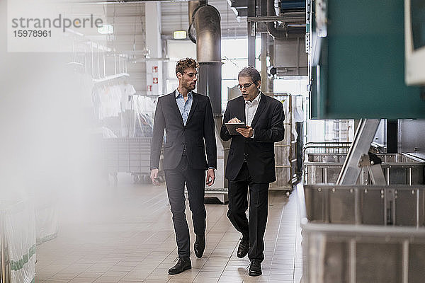 Zwei Geschäftsleute mit Tablette zu Fuß in einer Fabrik