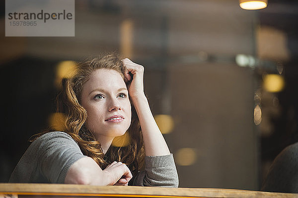 Nachdenkliche Frau  die sich auf einen Tisch stützt  gesehen durch ein Glasfenster in einem Café