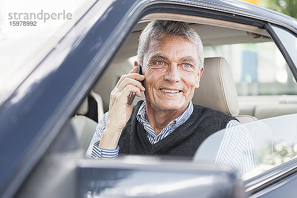 Porträt eines lächelnden älteren Geschäftsmannes beim Telefonieren im Auto