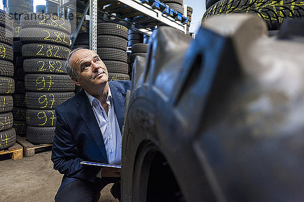 Selbstbewusster älterer Geschäftsmann  der aufblickt  während er in einem Geschäft neben einem Reifen hockt