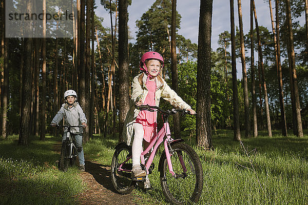 Mädchen und Junge fahren mit dem Fahrrad auf einem Fußweg im Wald