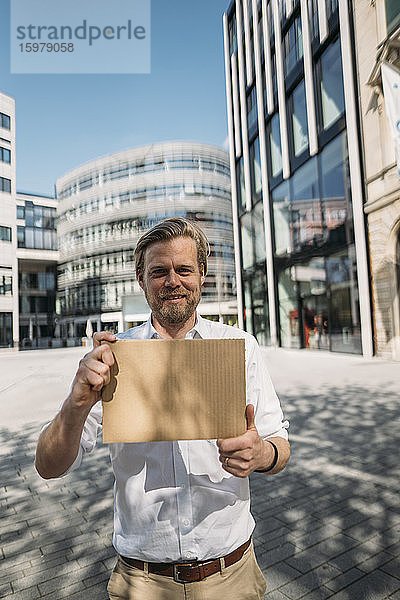Porträt eines lächelnden Mannes mit leerem Karton in der Stadt