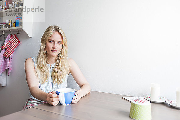 Porträt einer blonden jungen Frau  die am Tisch in der Küche sitzt
