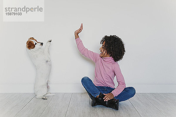 Lächelndes kleines Mädchen  das mit seinem Hund auf dem Boden sitzt