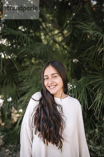 Porträt eines lächelnden Teenagers  der im Park vor einer Palme steht