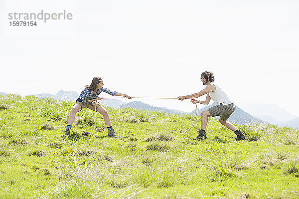 Mid adult couple pulling rope while competing in tug-of-war on mountain against clear sky