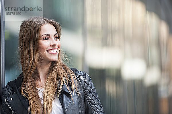 Nachdenkliche junge Frau lächelt  während sie an einem sonnigen Tag wegschaut