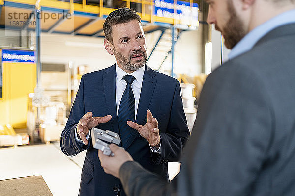 Zwei Geschäftsleute treffen sich in einer Fabrik und diskutieren über Werkstücke.