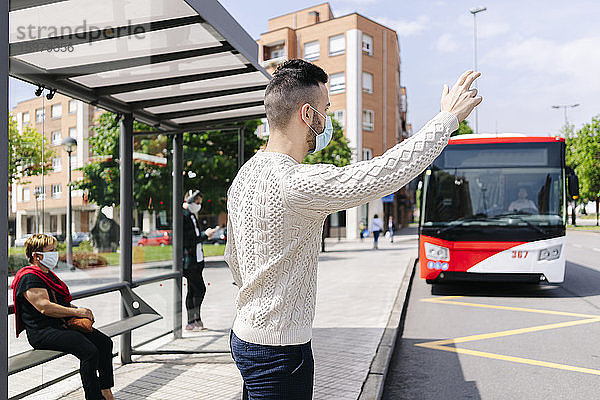 Mann mit Schutzmaske steht an einer Bushaltestelle und ruft ein Taxi  Spanien