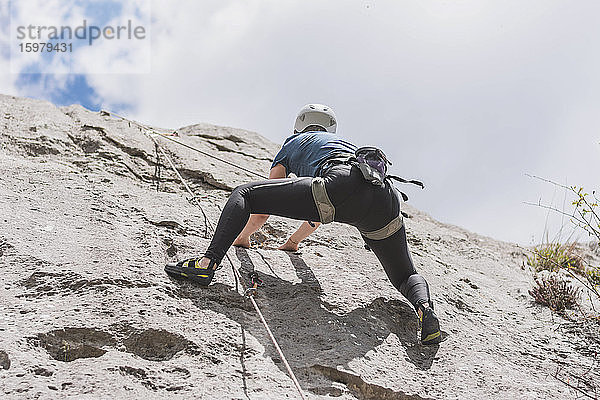 Junge Frau beim Klettern auf einem Felsen gegen den Himmel