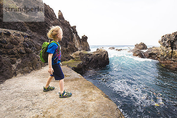 Junge in voller Länge  der auf einer Felsformation steht  während er das Meer an der Costa Adeje  Kanarische Inseln  Spanien  erkundet