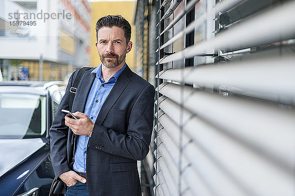 Porträt eines selbstbewussten Geschäftsmannes mit Smartphone in der Stadt