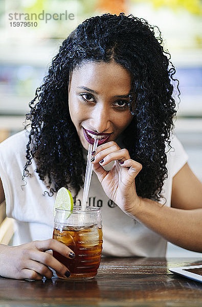 Porträt einer lächelnden jungen Frau  die am Tisch im Restaurant sitzt und trinkt