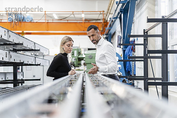 Geschäftsmann und Frau prüfen Metallstangen in einer Fabrikhalle