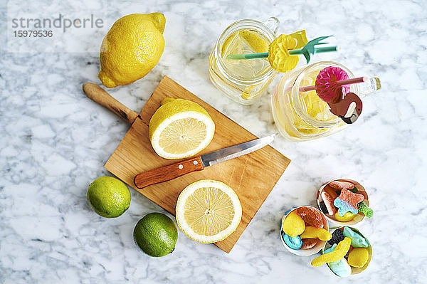 Schneidebrett  Küchenmesser  Zitronen  Limetten  Gummibonbons und Gläser mit frischer  selbstgemachter Limonade