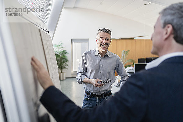 Glücklicher gut aussehender Geschäftsmann  der mit einem männlichen Kollegen in einer Besprechung im Büro eine Strategie am Whiteboard diskutiert