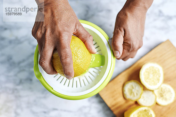 Hände einer Frau beim Auspressen von Zitronen mit einer Saftpresse